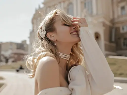 Uśmiechnięta blondynka w perłowej biżuterii, z perłową spinką we włosach. Masa perłowa znaczenie symbolizuje czystość i piękno.