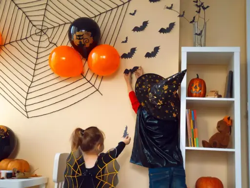 Dzieci w strojach na Halloween dekorują pokój, wieszając nietoperze na ścianie z wielką pajęczyną.