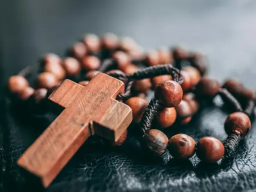 Drewniany krzyż i paciorki różańca, symbol wiary i modlitwy. Jeden dziesiątek różańca leży na ciemnym tle.