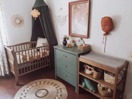 Przytulny pokój dziecka boho z drewnianym łóżeczkiem, przewijakiem i zieloną komodą. Dekoracje w stylu boho tworzą ciepłą atmosferę.