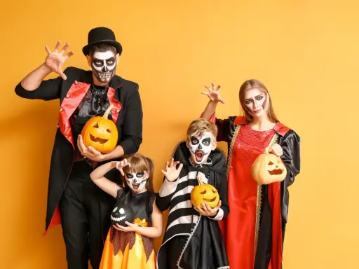 Rodzina w strojach na Halloween z dyniami i makijażem czaszki na żółtym tle.