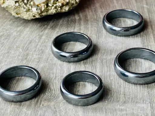 Pięć błyszczących, ciemnoszarych pierścionków z hematytu na drewnianym tle. Jak rozpoznać hematyt? Po jego metalicznym połysku i ciężarze.