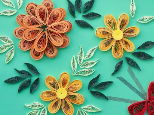 Kwiaty z papieru wykonane techniką quilling dla początkujących. Pomarańczowe, żółte i czerwone kwiaty oraz zielone i białe listki na turkusowym tle.