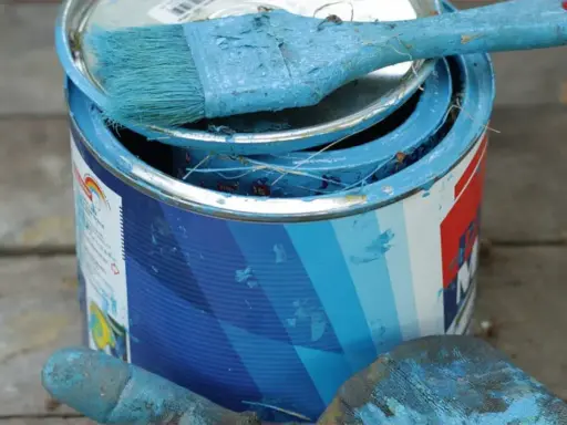 Puszka z niebieską farbą plakatową, pędzel i rękawica pokryte farbą.