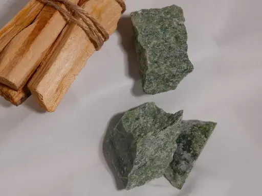 Surowe kawałki jadeitu w odcieniach zieleni, obok wiązki drewna palo santo.