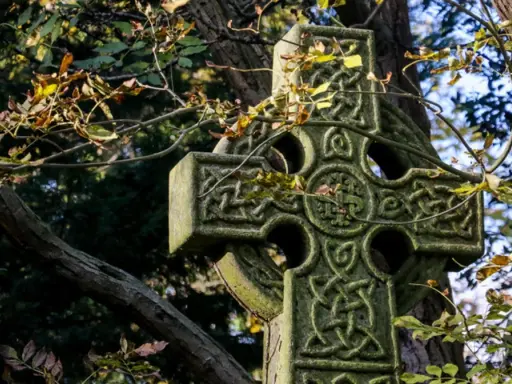 Kamienny krzyż celtycki z misternymi wzorami, otoczony jesiennymi liśćmi. Jego znaczenie symbolizuje wieczność i połączenie.