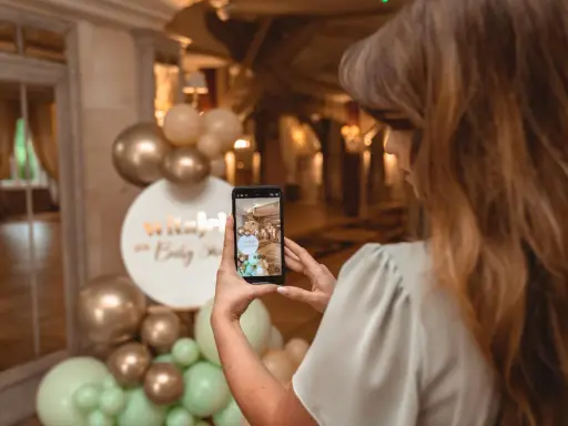 Kobieta robi zdjęcie dekoracji na baby shower. Złote i miętowe balony tworzą łuk. Świetne baby shower pomysły!