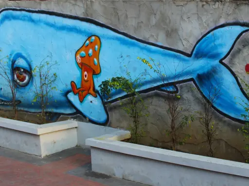Niebieski wieloryb z grzybkiem na grzbiecie. Inspiracja, jak zrobić mural na kartce, w miejskim krajobrazie.