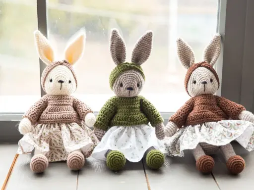 Trzy szydełkowe króliczki w sukienkach i czapeczkach, siedzące obok siebie.