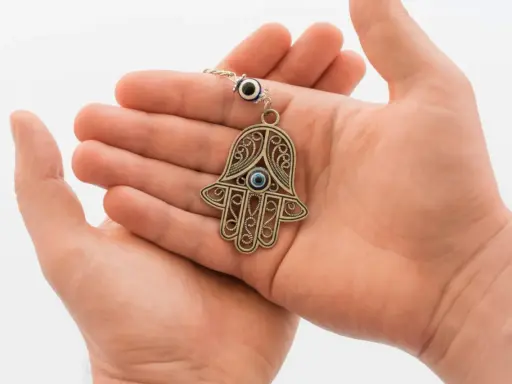 Dłonie trzymające ozdobny amulet w kształcie ręki Fatimy z niebieskim okiem.