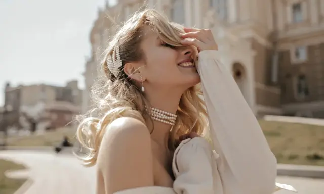 Uśmiechnięta blondynka w perłowej biżuterii, z perłową spinką we włosach. Masa perłowa znaczenie symbolizuje czystość i piękno.