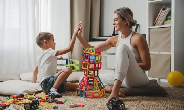 Mama i syn świętują sukces kreatywnych zabaw plastycznych, budując wieżę z kolorowych klocków.