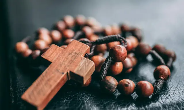 Drewniany krzyż i paciorki różańca, symbol wiary i modlitwy. Jeden dziesiątek różańca leży na ciemnym tle.