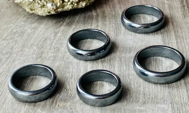Pięć błyszczących, ciemnoszarych pierścionków z hematytu na drewnianym tle. Jak rozpoznać hematyt? Po jego metalicznym połysku i ciężarze.