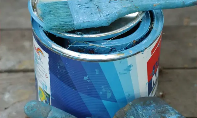 Puszka z niebieską farbą plakatową, pędzel i rękawica pokryte farbą.