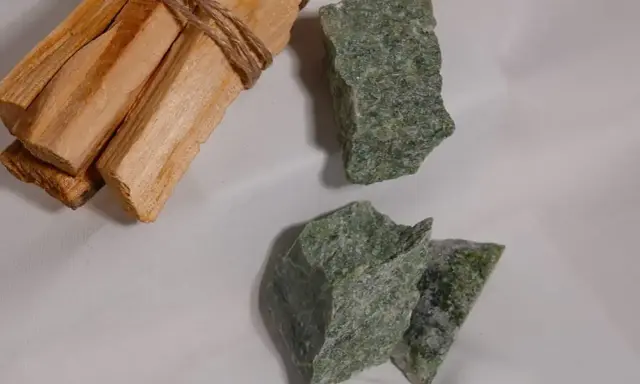 Surowe kawałki jadeitu w odcieniach zieleni, obok wiązki drewna palo santo.