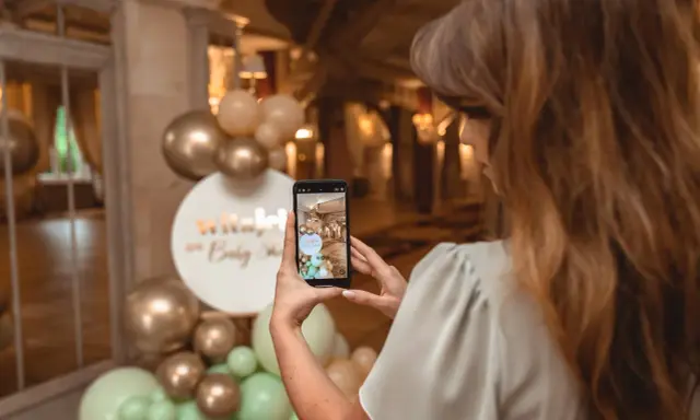 Kobieta robi zdjęcie dekoracji na baby shower. Złote i miętowe balony tworzą łuk. Świetne baby shower pomysły!