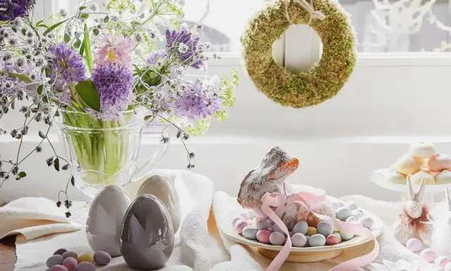 Wielkanocne dekoracje: bukiet wiosennych kwiatów, ceramiczne jajka, lukrowany zajączek otoczony cukierkami i mechowy wianek.