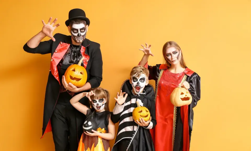 Rodzina w strojach na Halloween z dyniami i makijażem czaszki na żółtym tle.