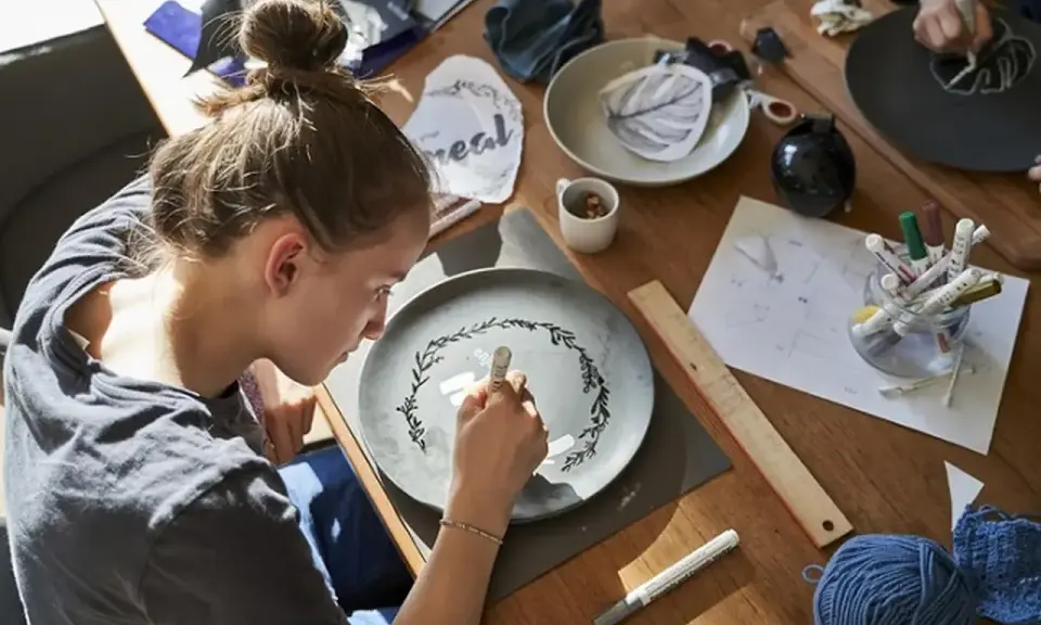 Dziewczyna maluje na talerzu, tworząc wzór. Wokół materiały do rękodzieła, jak do zimna porcelana przepis.