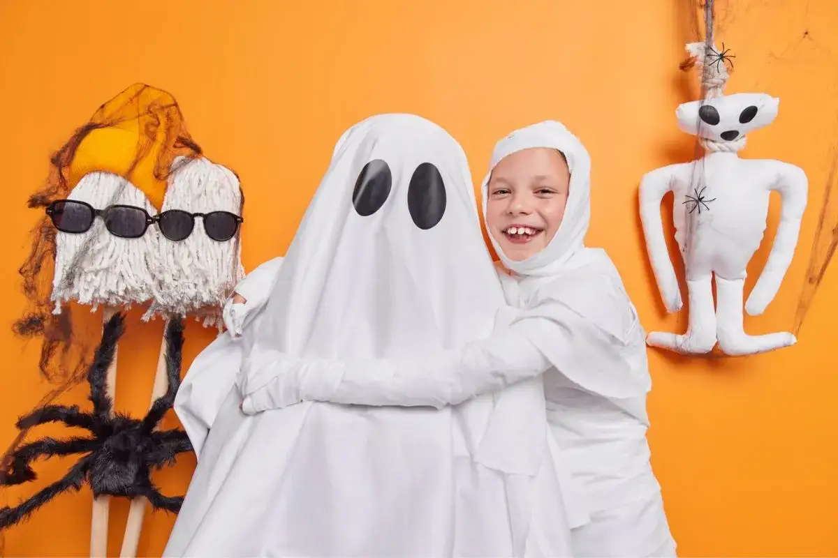 Dzieci w kostiumach mumii i ducha, świetny pomysł na kostium halloween. Obok pluszowy szkielet i pajęczyna.