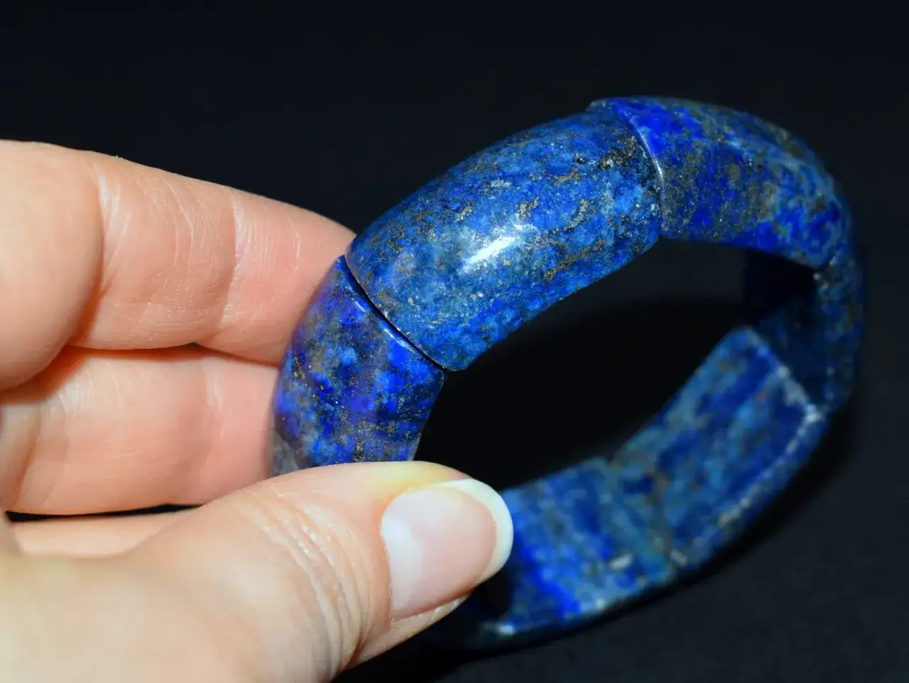 Błękitna bransoleta z lapis lazuli, gdzie każdy kamień z drobinkami złota lśni w świetle.