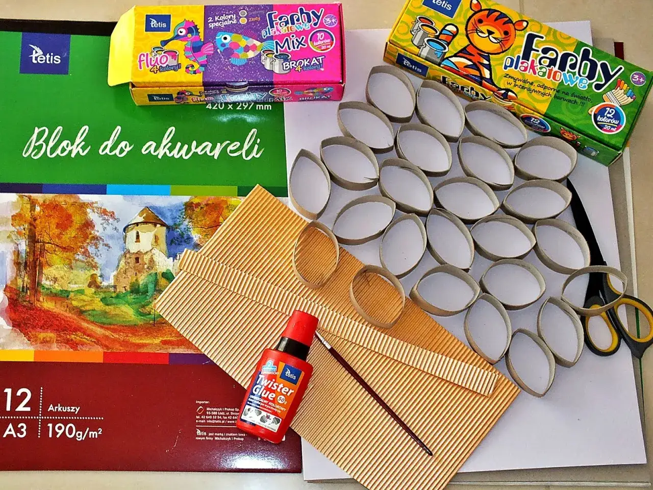 Materiały do tworzenia przestrzennej pisanki 3d: rolki po papierze, farby, klej, pędzelek, tektura i blok do akwareli.