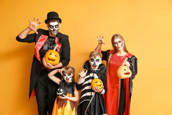 Rodzina w strojach na Halloween z dyniami i makijażem czaszki na żółtym tle.