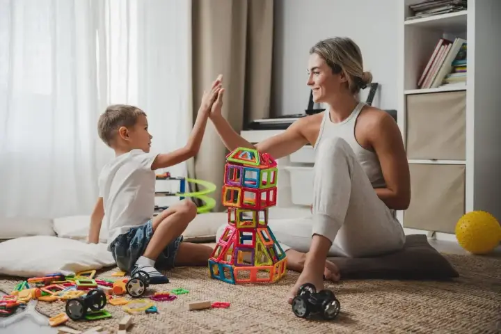 Mama i syn świętują sukces kreatywnych zabaw plastycznych, budując wieżę z kolorowych klocków.