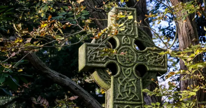 Kamienny krzyż celtycki z misternymi wzorami, otoczony jesiennymi liśćmi. Jego znaczenie symbolizuje wieczność i połączenie.